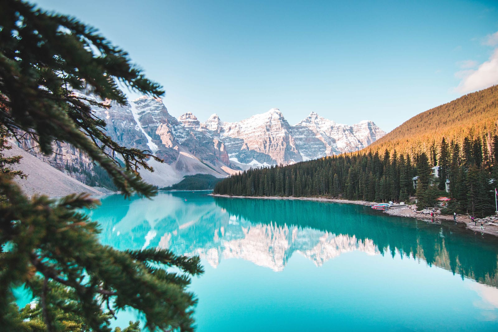 A stunning turquoise alpine lake surrounded by snow-capped Rocky Mountains and dense evergreen forest. The pristine waters perfectly reflect the rugged mountain peaks in Banff National Park, Canada.