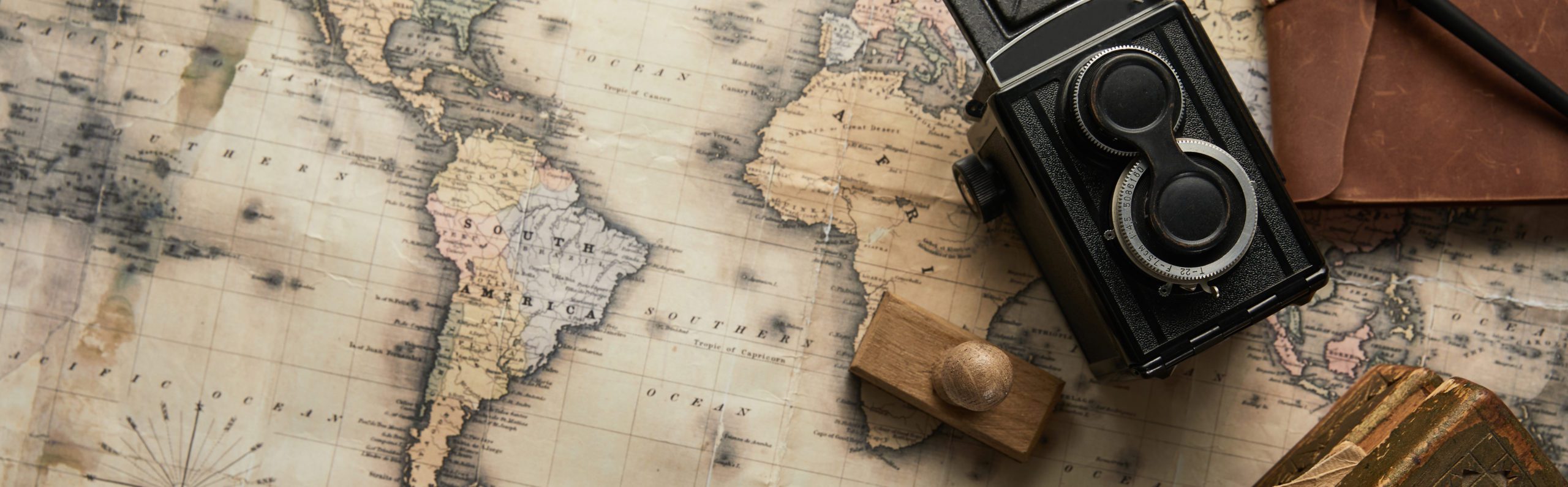 An antique map of South America with a vintage twin-lens reflex camera positioned alongside, suggesting themes of travel, exploration, and cartography.
