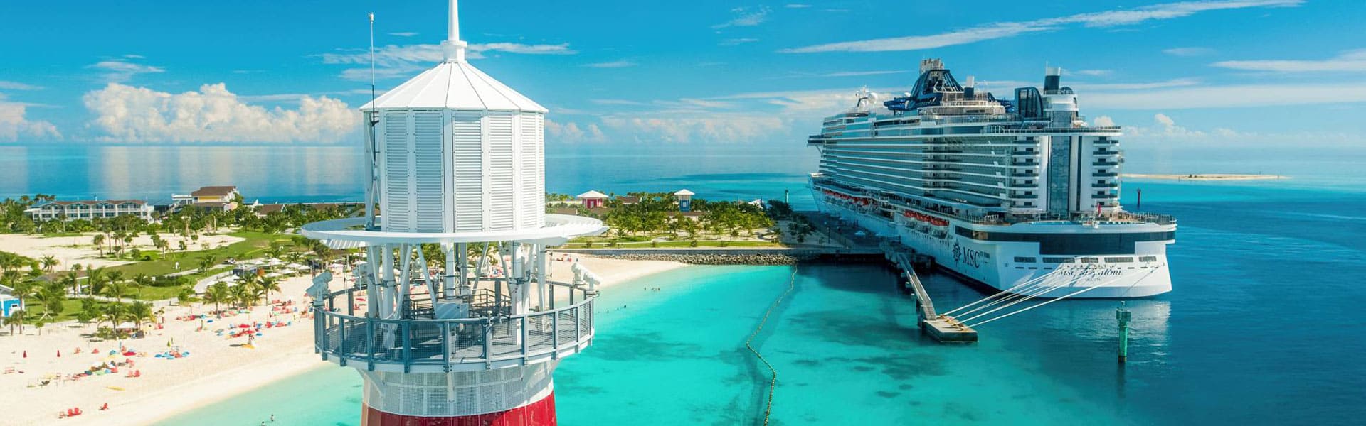 A large MSC cruise ship docked at the pristine Ocean Cay marine reserve in the Bahamas, with a white lighthouse and turquoise waters surrounding a white sandy beach.