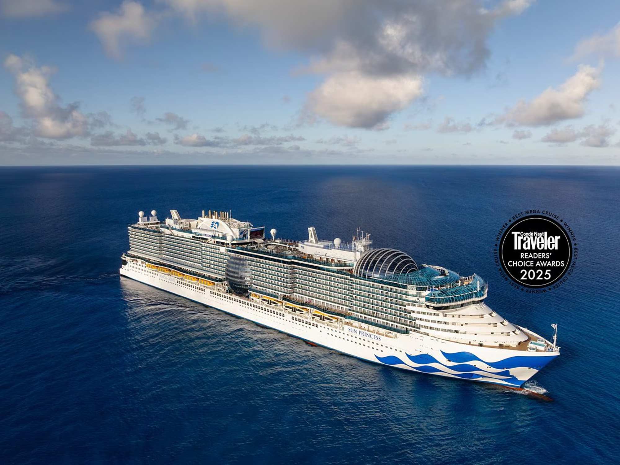 Sun Princess Mega Cruise Ship at Sea A large modern cruise ship sailing on deep blue ocean waters under a cloudy sky, featuring a sleek white and blue design with multiple decks and a distinctive glass dome structure.