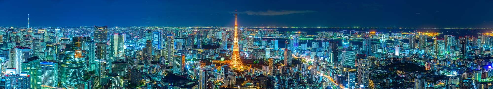 A stunning panoramic view of Tokyo's cityscape at night, featuring the iconic Tokyo Tower illuminated in orange amid dense, glowing skyscrapers and urban landscape.